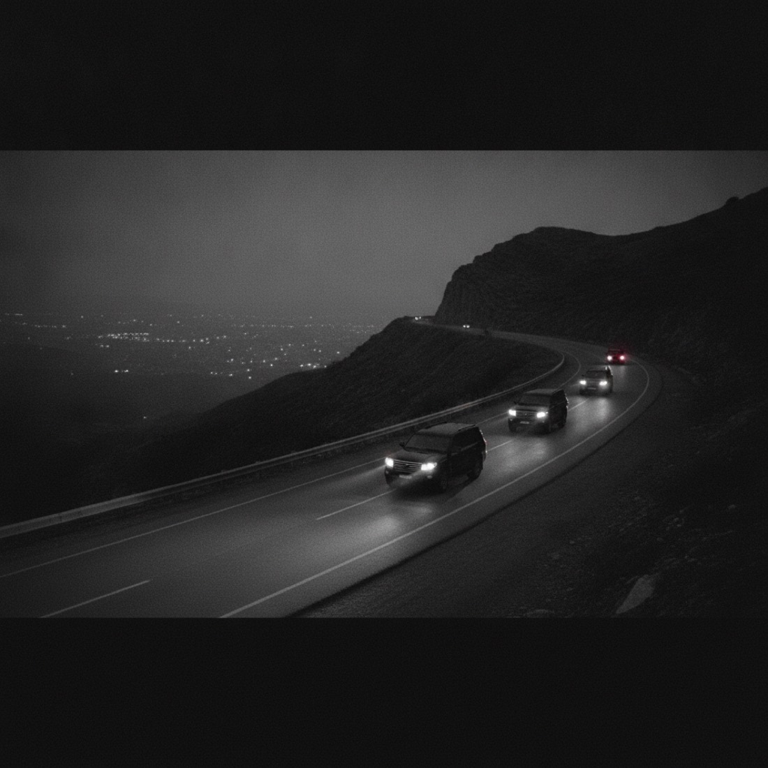 Three black SUVs in convoy on a mountain road at dusk